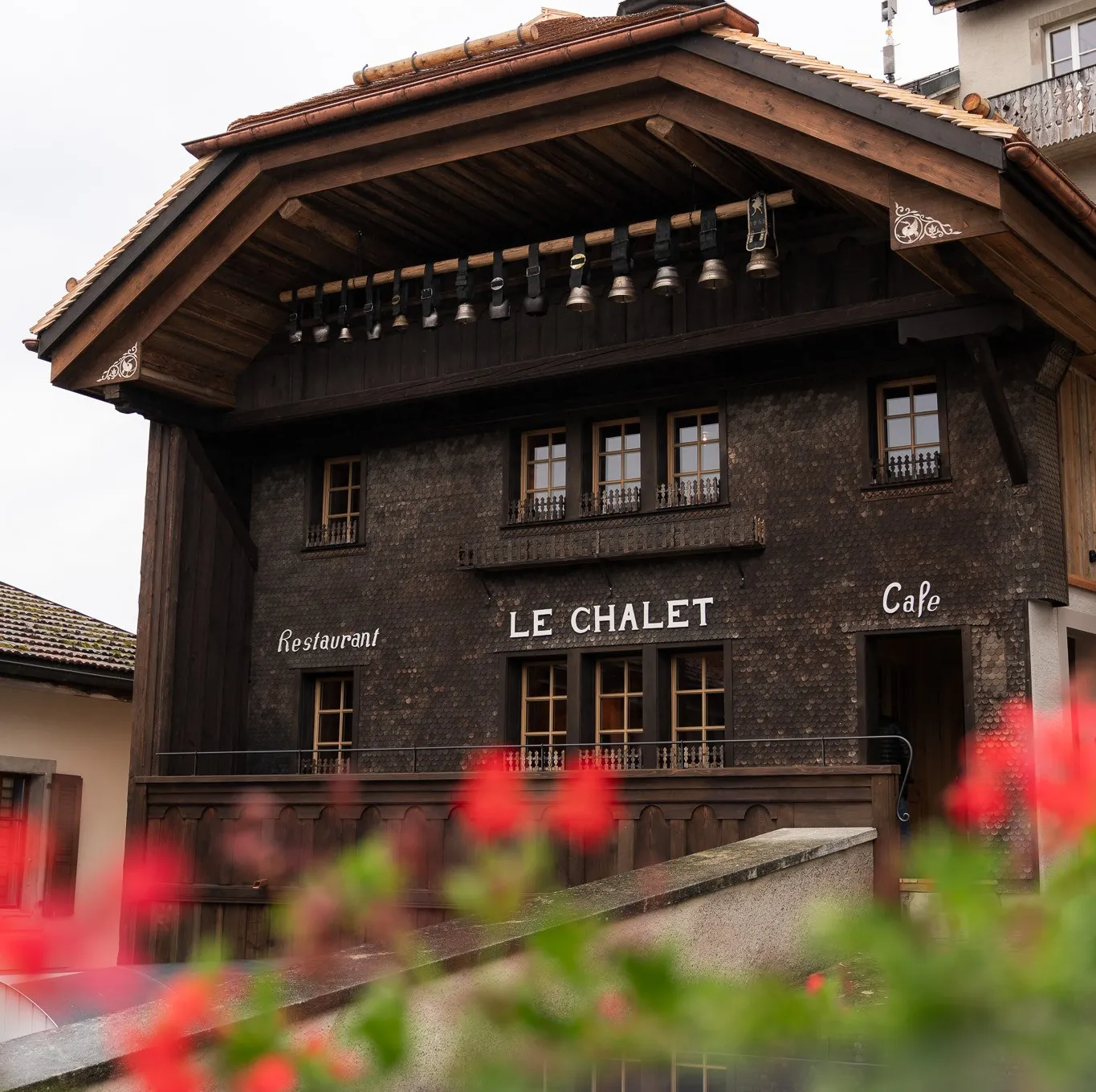 La façade en bois sombre du Chalet de Gruyères, Rue du Bourg, et ses géraniums rouges