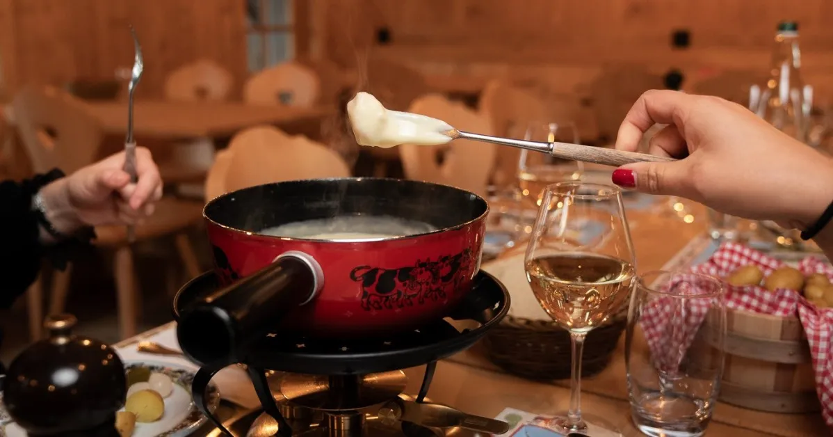 Caquelon de fondue rouge sur son réchaud, fourchettes et verre de vin blanc